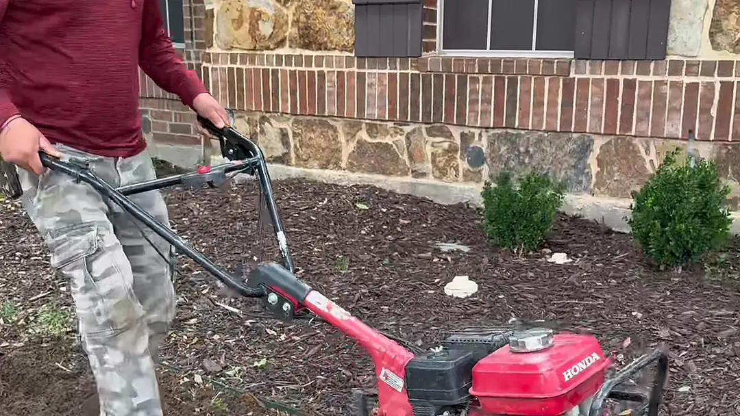 Crew member tilling a planting bed in front of a stone and brick home